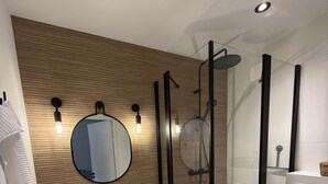 A modern bathroom with a wooden wall, a round mirror, two sinks, a glass-enclosed shower, and a toilet. - Gîte TI BOEM, near Cancale, Saint-Malo and Mont-Saint-Michel (La Fresnais)
