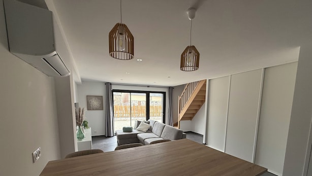 A modern living room with a wooden dining table, a sofa, and a staircase leading to an upper level. - Gîte TI BOEM, near Cancale, Saint-Malo and Mont-Saint-Michel (La Fresnais)