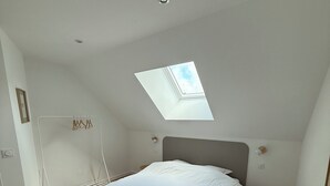 A bedroom with a skylight, a bed, a small table, and a drying rack. - Gîte TI BOEM, near Cancale, Saint-Malo and Mont-Saint-Michel (La Fresnais)