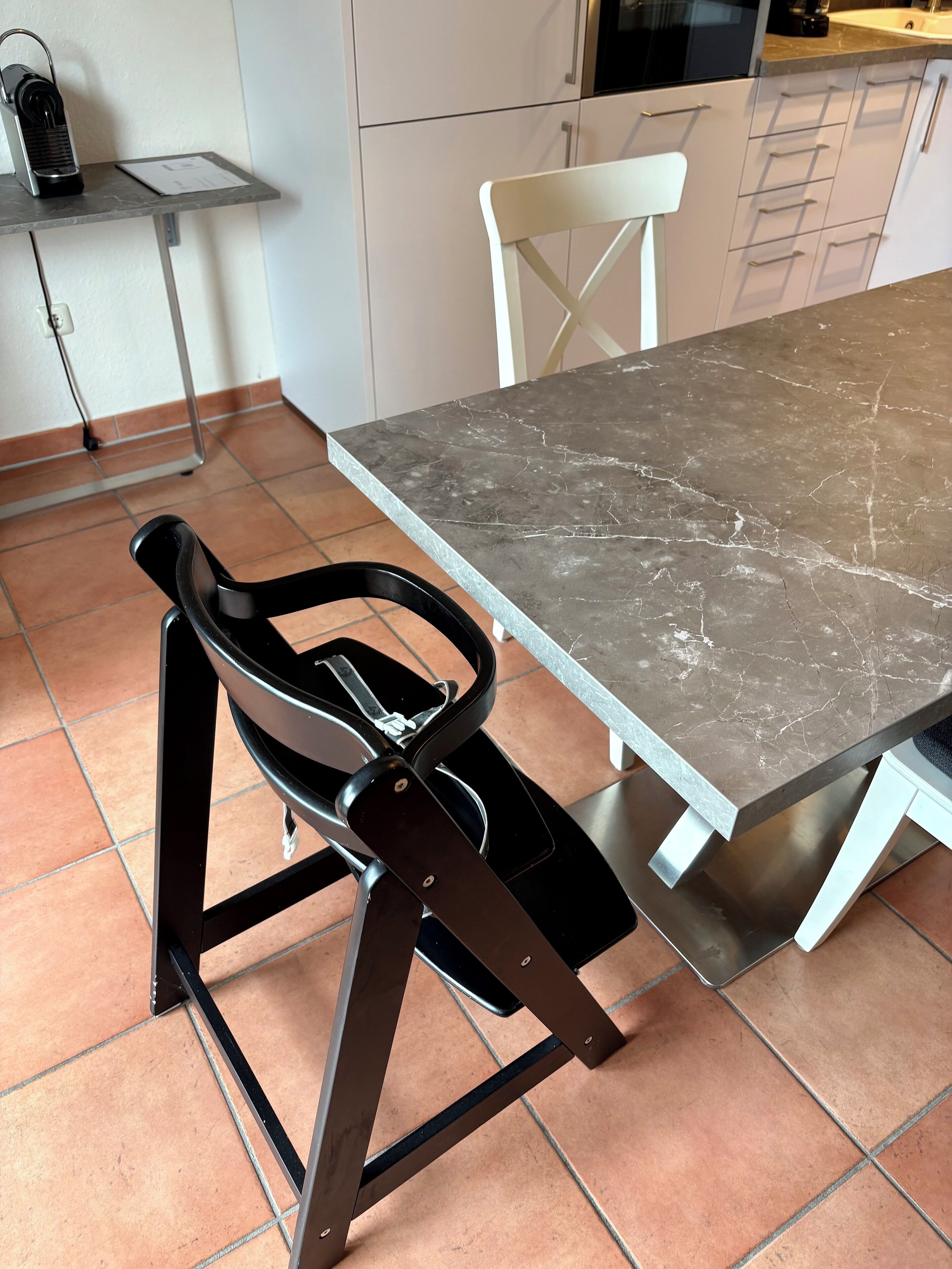 Een eettafel met een marmeren blad, een zwarte stoel met metalen frame en een witte stoel met metalen frame.
