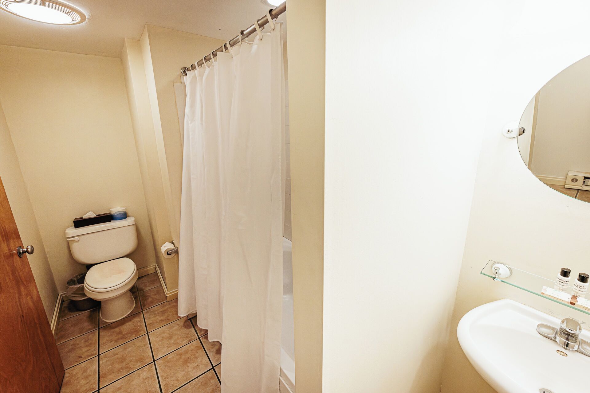 Un baño con inodoro, cortina de ducha y lavamanos con espejo.