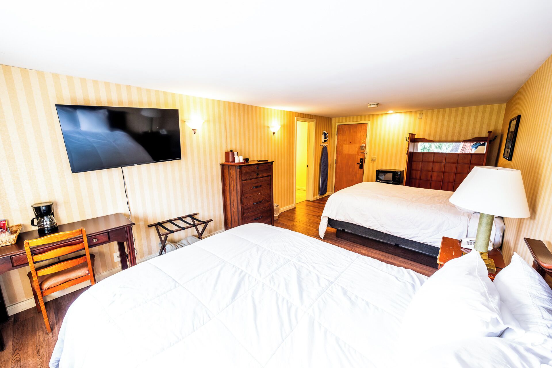 Habitación de hotel con dos camas, televisión, escritorio con silla, cómoda y microondas.