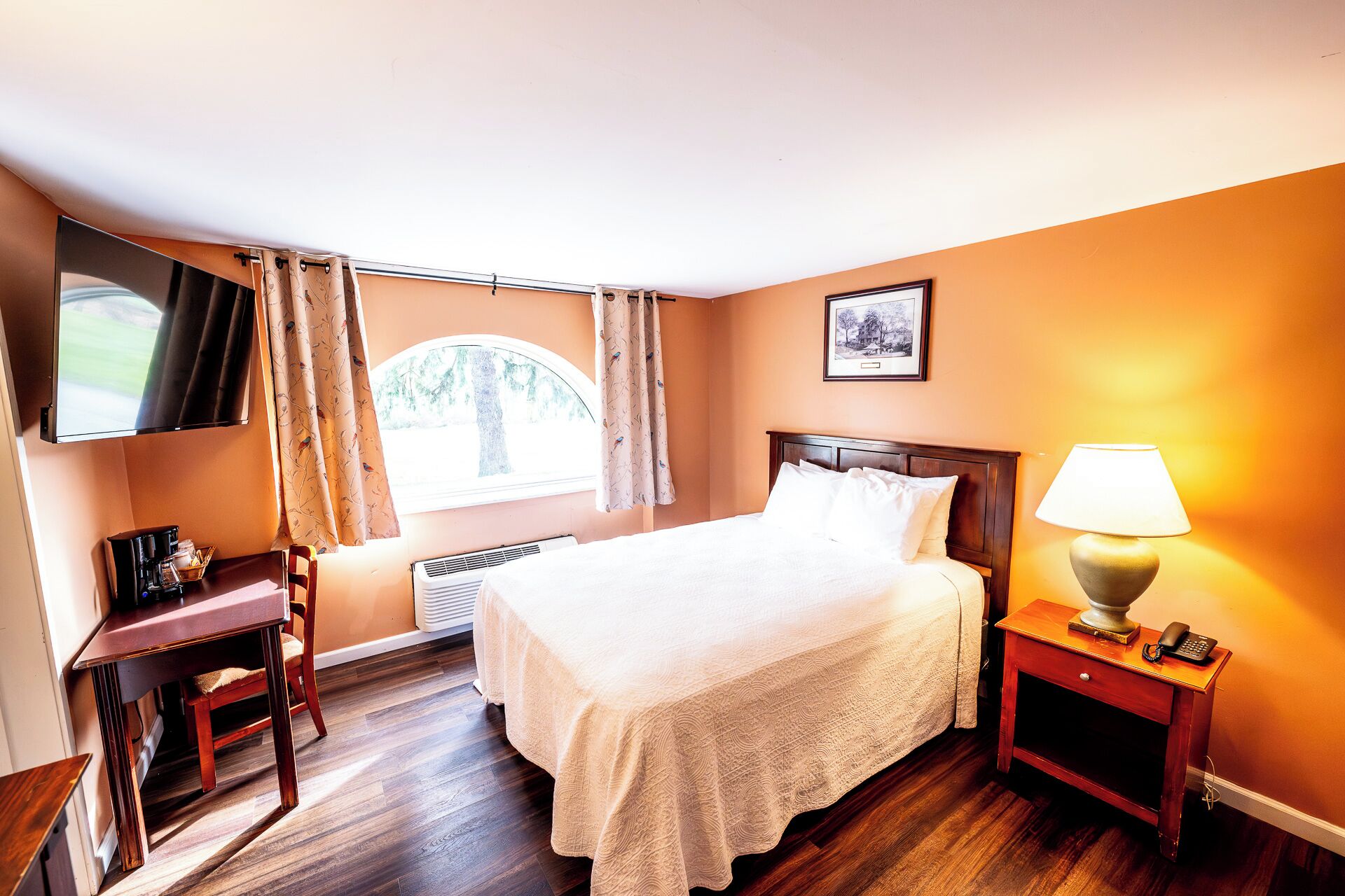 A hotel room with a bed, a desk, a chair, a lamp, and a picture on the wall.