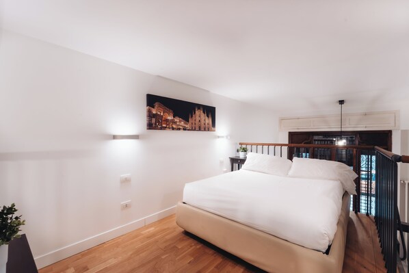 A bedroom with a large bed, a nightstand, a painting of a building, and a view of a balcony with a railing. - charming de togni apartment (Milan)