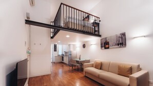 Ein modernes Wohnzimmer mit Holzboden, einem beigefarbenen Sofa und einer Treppe, die zu einer oberen Ebene führt.