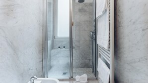 Ein modernes Badezimmer mit einer Glastrennwand-Dusche, Marmorwänden und einem sichtbaren Fenster.