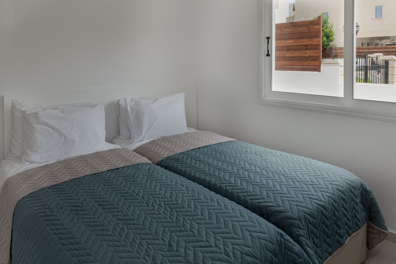 A bedroom with two beds, white bedding, and a window with a view of the outside.