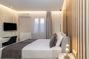 A modern hotel room with a bed, a desk, a flat-screen TV, and a bedside table.