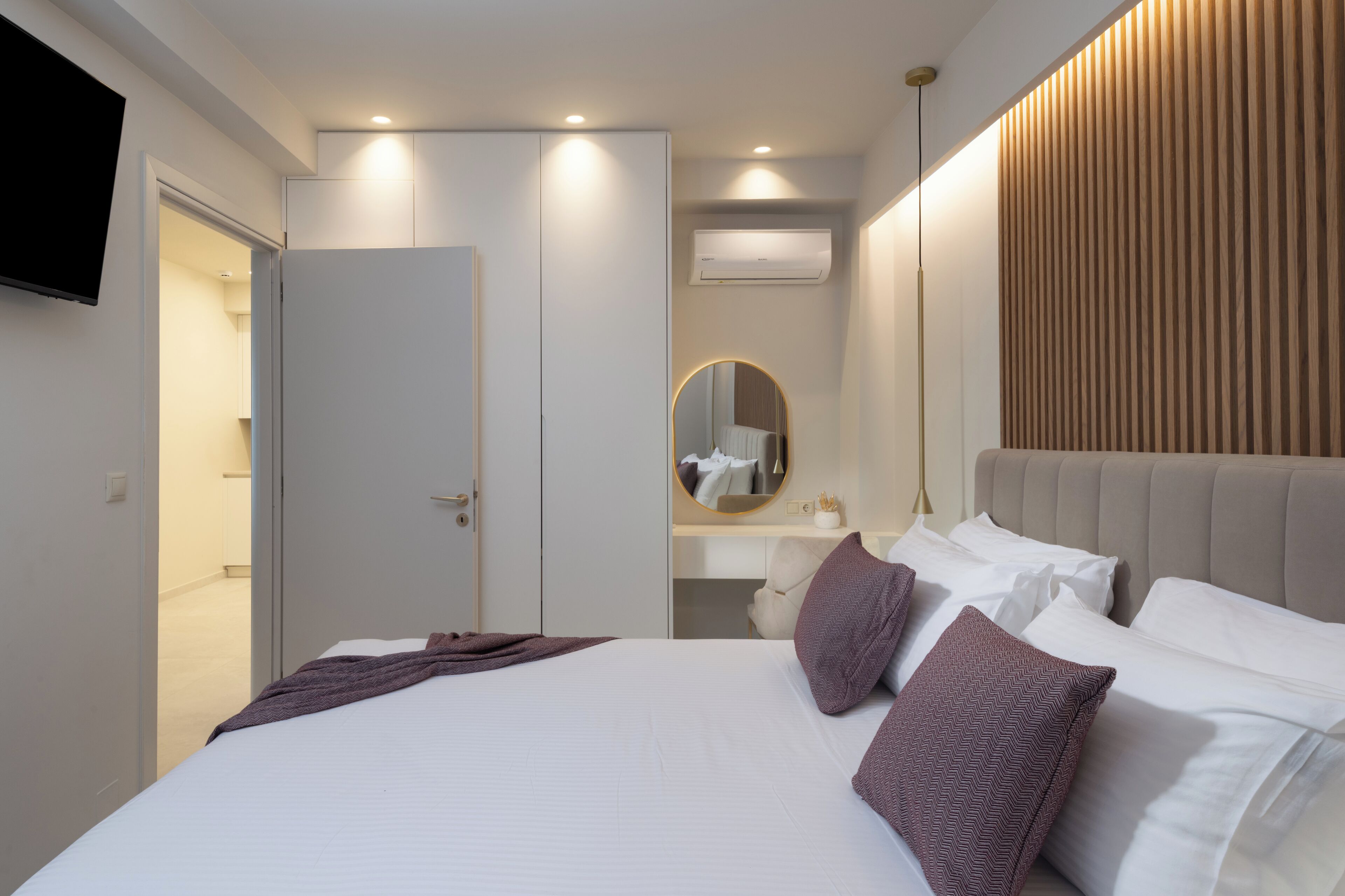 Un dormitorio moderno con una cama grande, una mesita de noche, un espejo y un televisor montado en la pared.