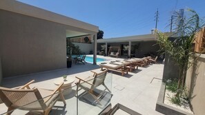 A poolside area with lounge chairs and a glass table, surrounded by a modern building with a covered patio.