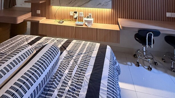 Une chambre moderne avec un grand lit, un bureau, une chaise, un téléviseur fixé à un mur en bois et une petite étagère avec des plantes.