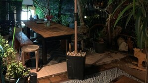 An outdoor patio area with a wooden table and benches, a large umbrella, and potted plants. - Large studio with garden: a haven of freshness and greenery right in the center of town (Cavalaire-sur-Mer)