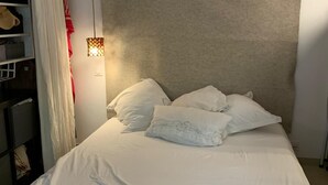 A neatly made bed with white bedding, a headboard, and a hanging light fixture. - Large studio with garden: a haven of freshness and greenery right in the center of town (Cavalaire-sur-Mer)