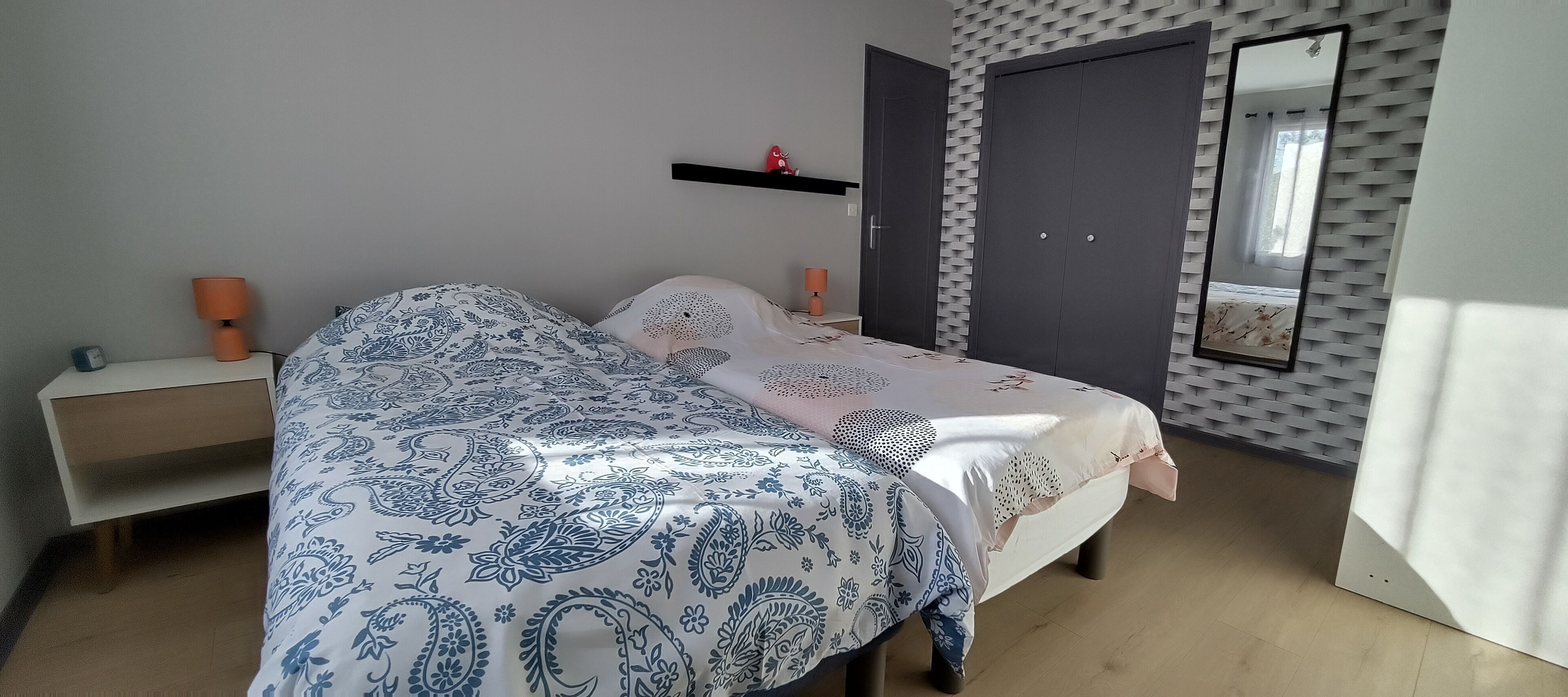 Une chambre à coucher comprenant un lit, des tables de chevet, une armoire, un miroir et un mur orné d’un motif texturé.