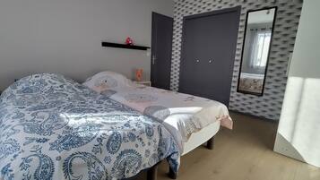 Une chambre à coucher comprenant un lit, des tables de chevet, une armoire, un miroir et un mur orné d’un motif texturé.