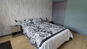 Um quarto com cama, mesa de cabeceira, abajur e guarda-roupa.