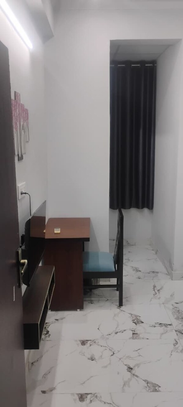 A small room with a desk and chair, a dark curtain, and a white tiled floor. - Hotel Sefra (Jaipur)