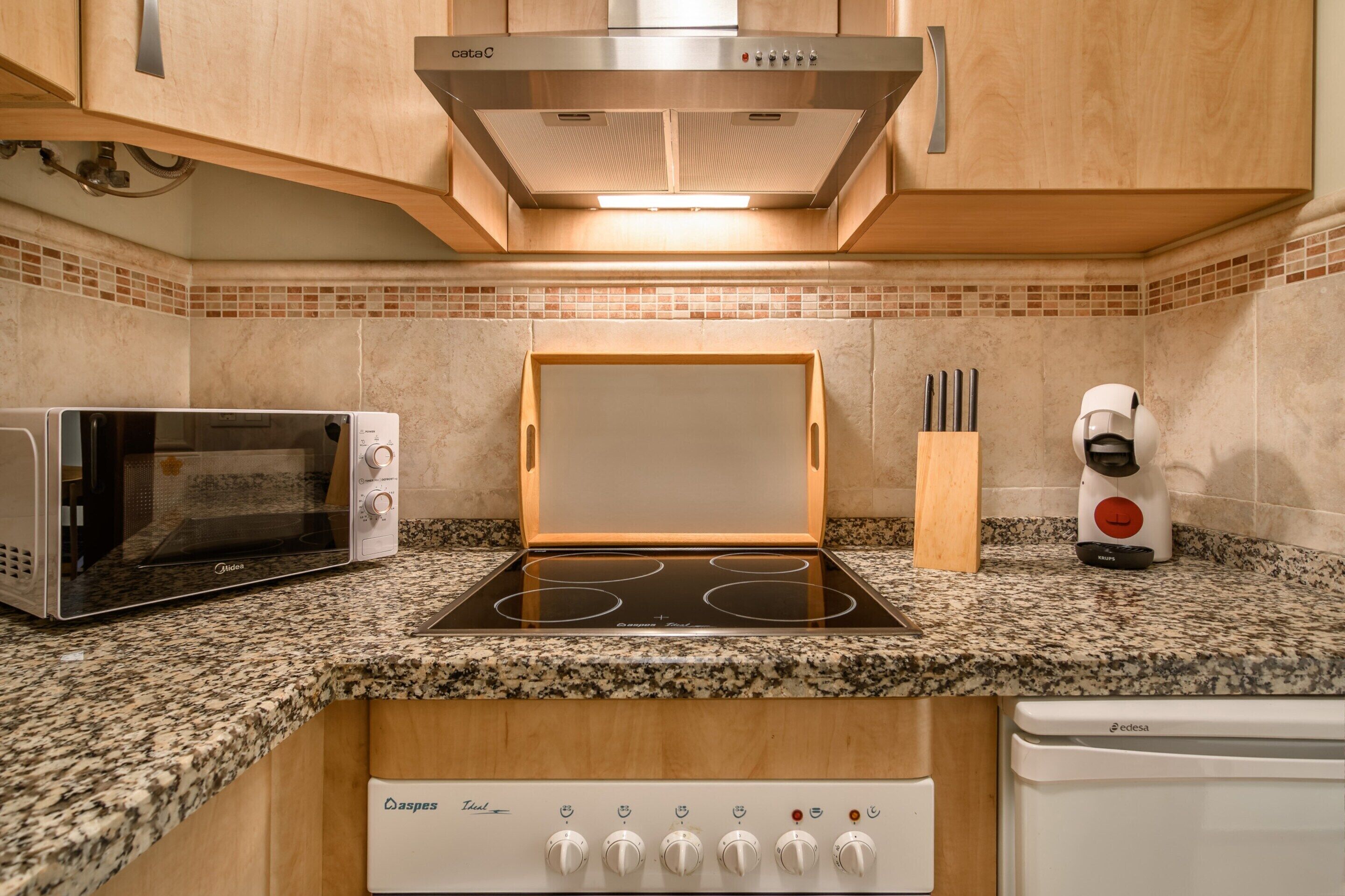 Une cuisine équipée d’un four à micro-ondes encastré, d’une plaque de cuisson et d’un lave-vaisselle.