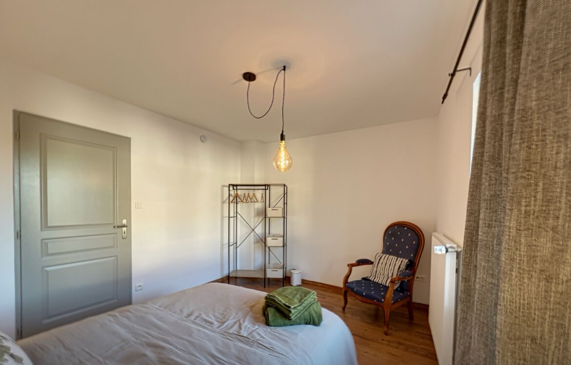 A bedroom with a bed, a chair, a radiator, and a hanging light fixture.