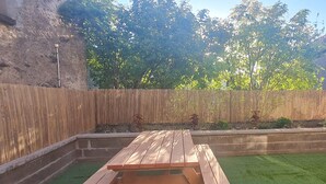 A wooden picnic table in a garden with a stone wall and green grass.