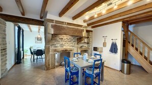 A rustic dining area with a stone fireplace, wooden beams, and a tiled floor.