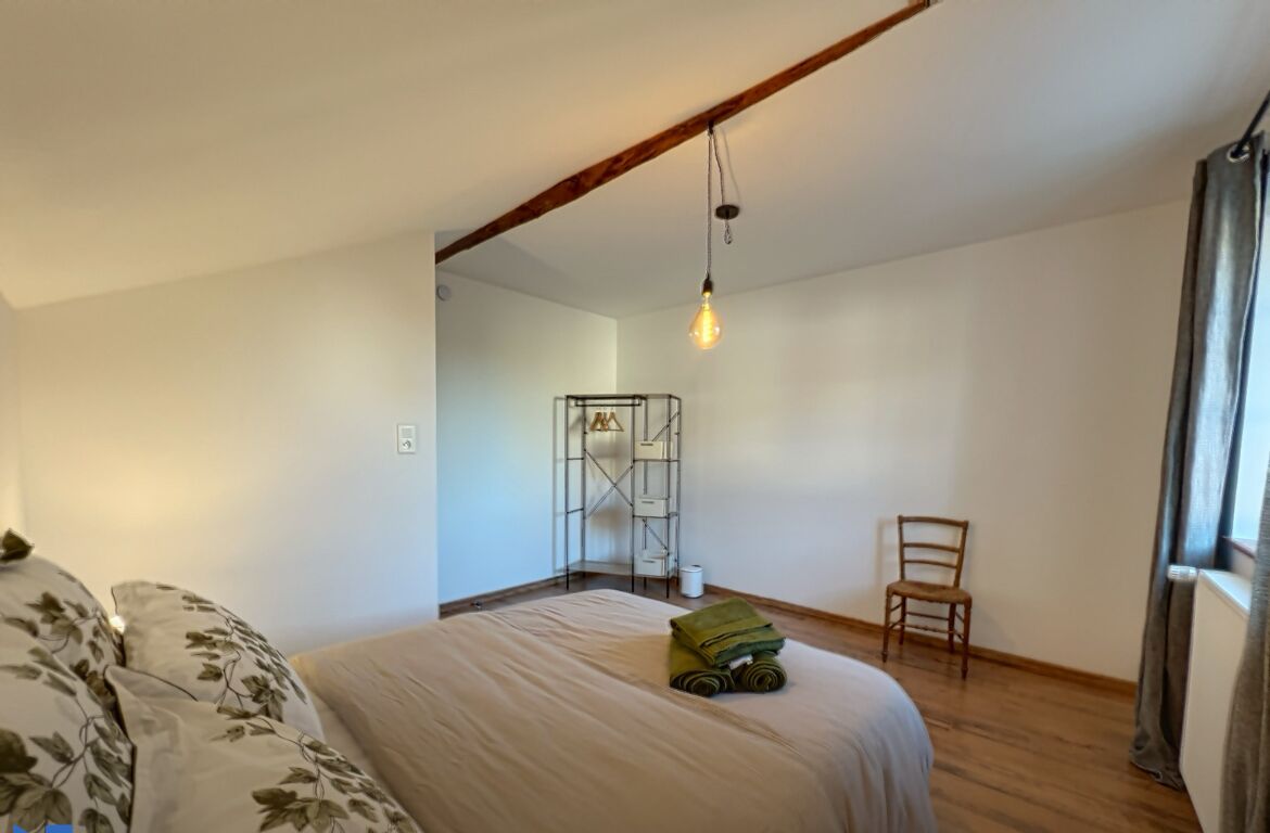 Une chambre à coucher comprenant un lit, une chaise, un luminaire suspendu et une étagère en métal.