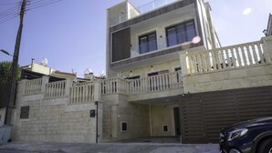 A two-story building with a balcony on the upper floor, a garage door on the ground floor, and a parked car in front. - Huge 5BR Villa with Rooftop Lounge/BBQ ZONE/PRIVATE POOL in delightful Chlorakas (Chlorakas)