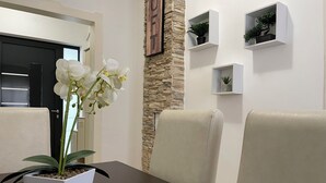 A dining area with a white orchid in a square pot, beige cushioned chairs, a dark wooden table, and a stone accent wall with a framed word above it. - Cozy & Stylish Townhouse in Central Niš w/ 2BR • WiFi • AC (Niš)