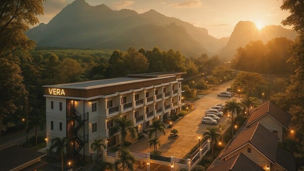 Un hotel de varios pisos con un llamativo letrero que dice "VERA", rodeado de exuberante vegetación y montañas al fondo.