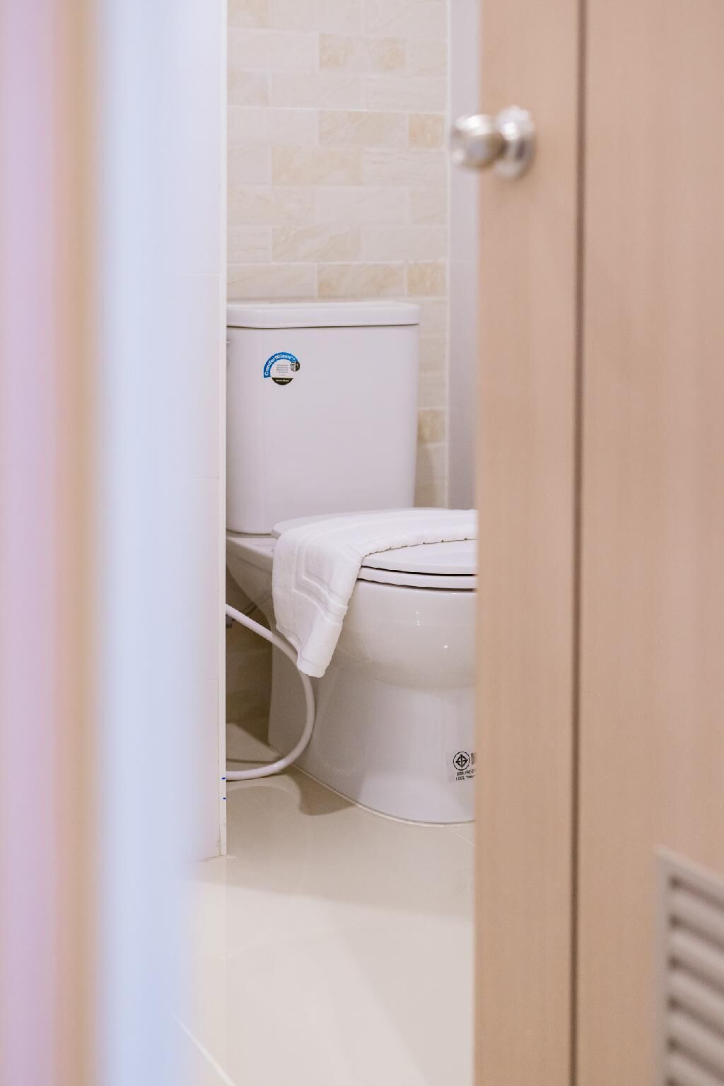 A bathroom with a toilet, a white tiled wall, and a door.