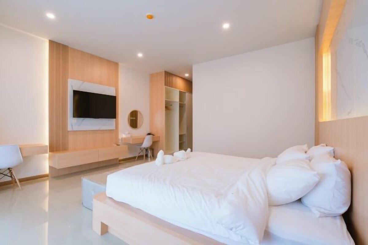A modern bedroom with a large bed, a TV mounted on the wall, a desk, and a walk-in closet.
