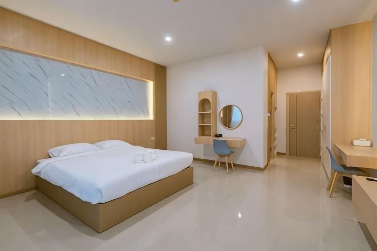 A modern bedroom with a large bed, a desk, a chair, and a mirror.