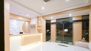 Una zona de recepción moderna con un mostrador de madera, un reloj y una puerta de vidrio que da al exterior.