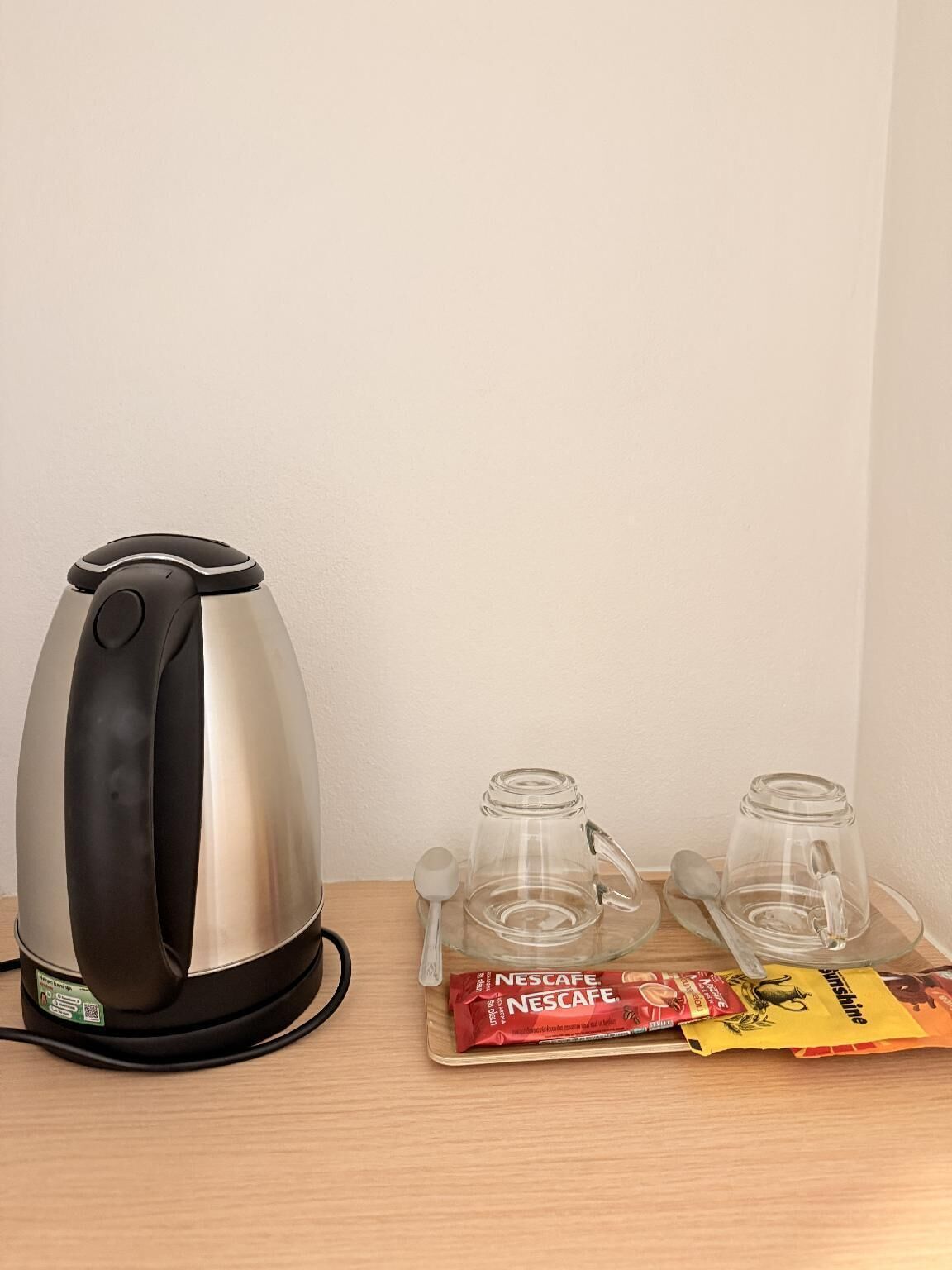 A coffee maker, two glass mugs, and two packets of Nescafe coffee on a wooden table.