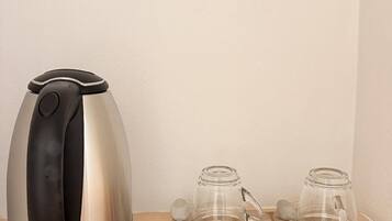 A coffee maker, two glass mugs, and two packets of Nescafe coffee on a wooden table.