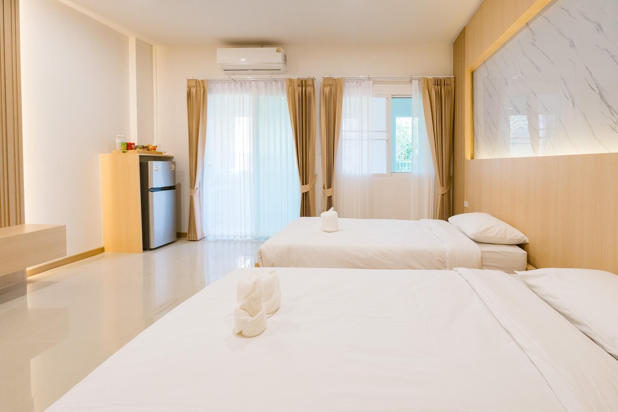 A hotel room with two beds, a minibar, and a large window with curtains.