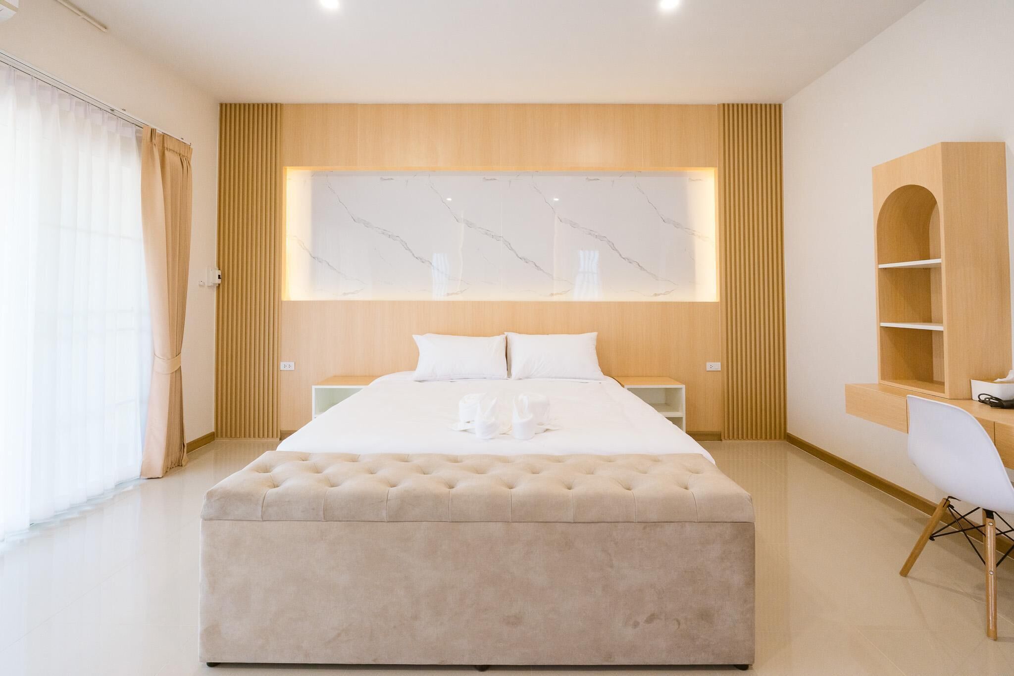 A modern bedroom with a large bed, a wooden headboard, a marble wall, and a built-in desk with a chair.