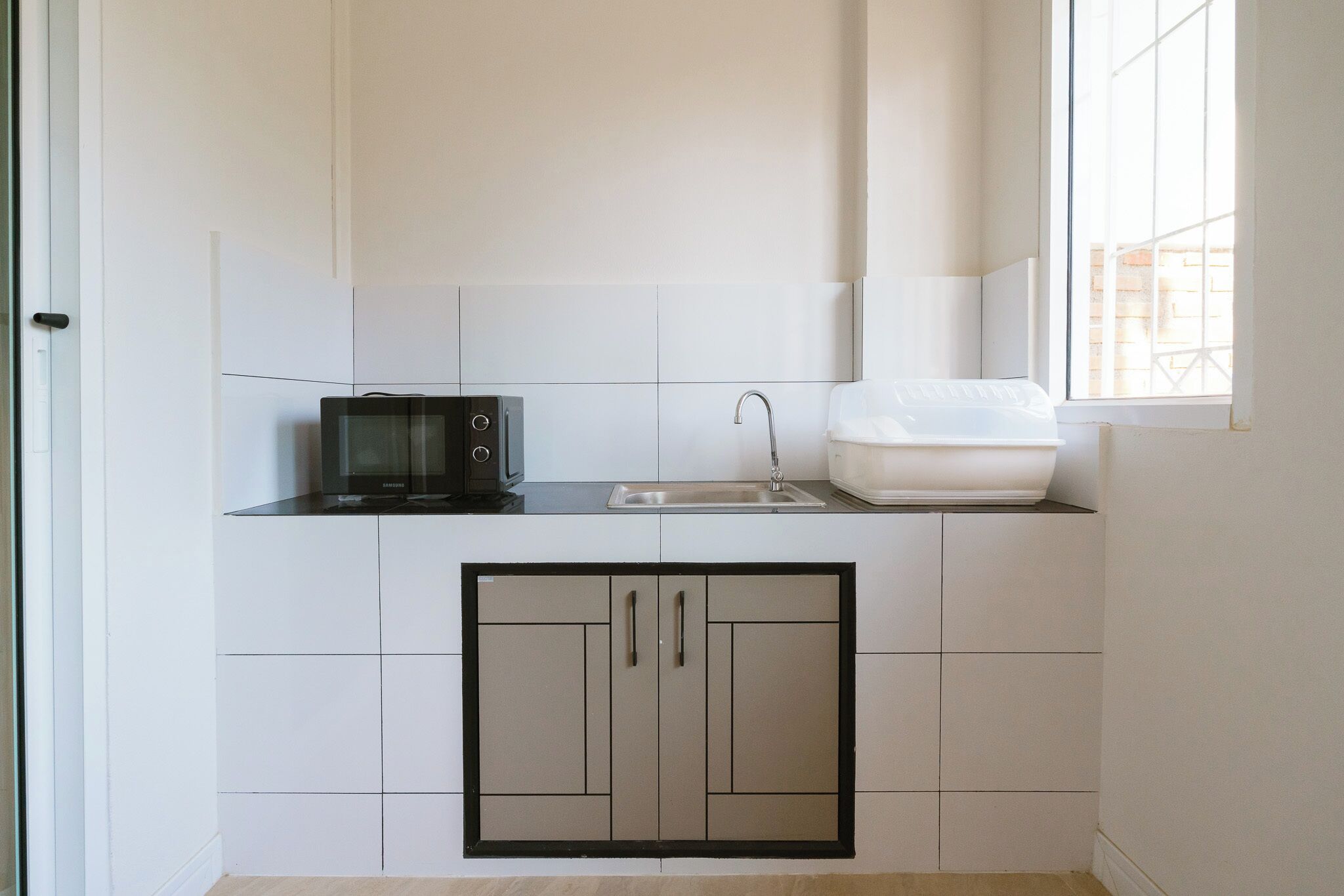 Una kitchenette compacta con microondas, lavamanos y espacio para guardar cosas en armarios.