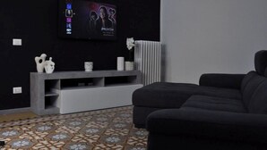 A modern living room with a grey sofa, a flat-screen TV mounted on the wall, a white console table with decorative items, and a patterned floor.