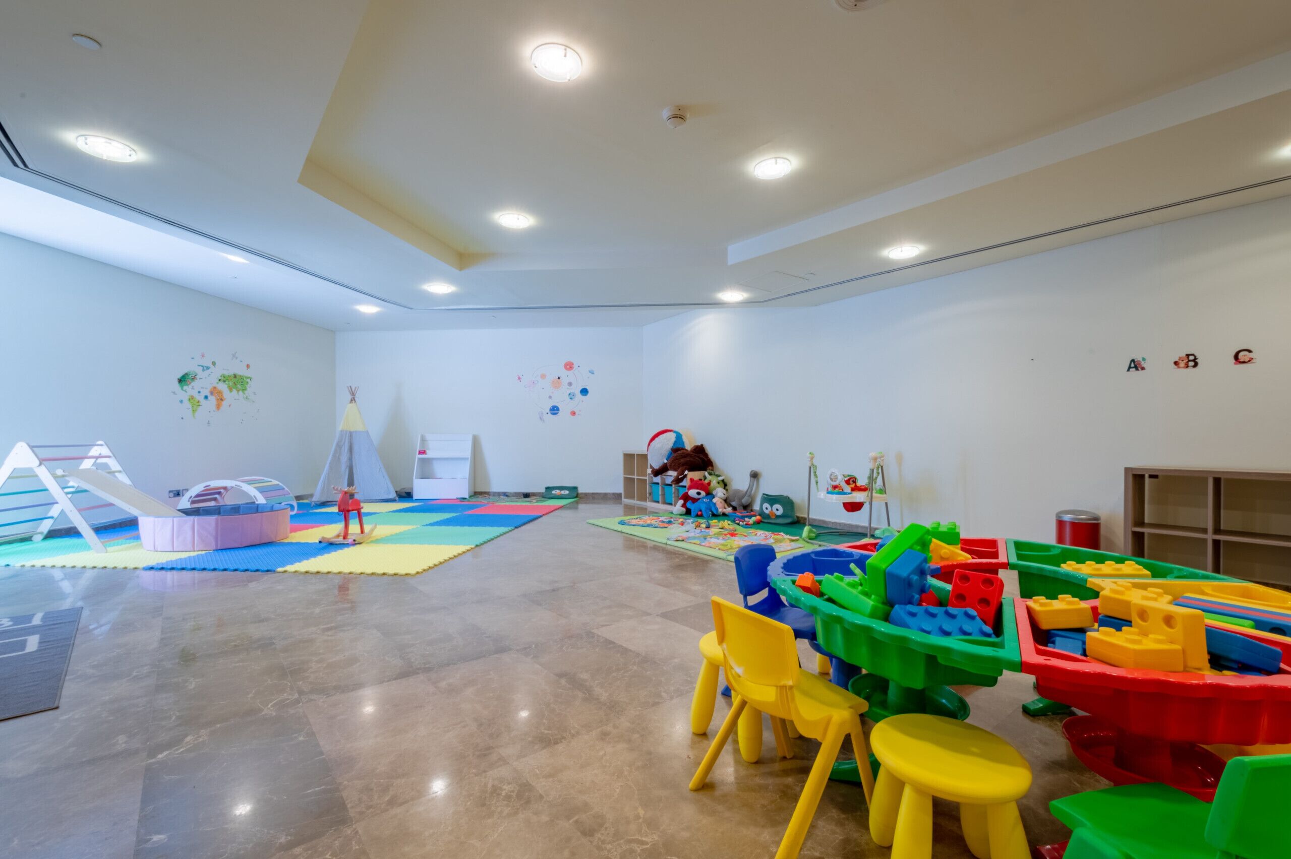 Una sala de juegos amplia con un área de juegos acolchada, juguetes coloridos y una casita.