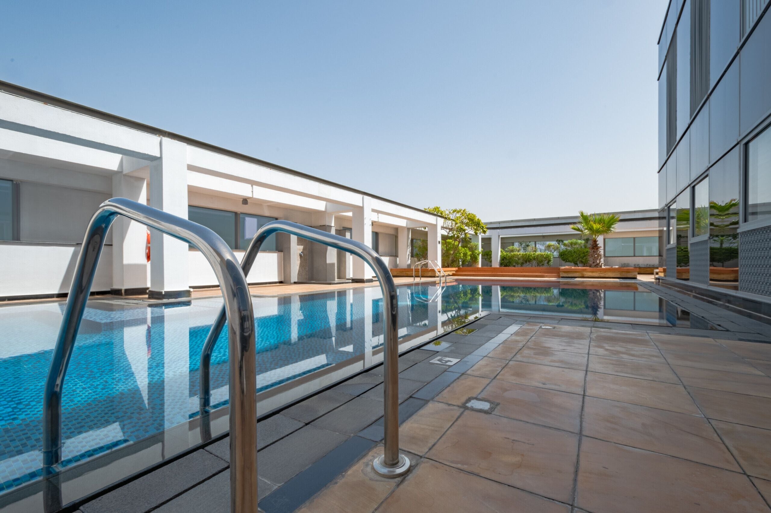 A modern outdoor pool area with clear blue water, metal pool ladders, and a tiled deck.