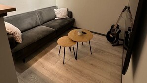 A modern living room with a dark grey sofa, two round wooden tables, a guitar, and a flat-screen TV mounted on the wall. - 2-bedroom apartment in Fredrikstad (Østfold)