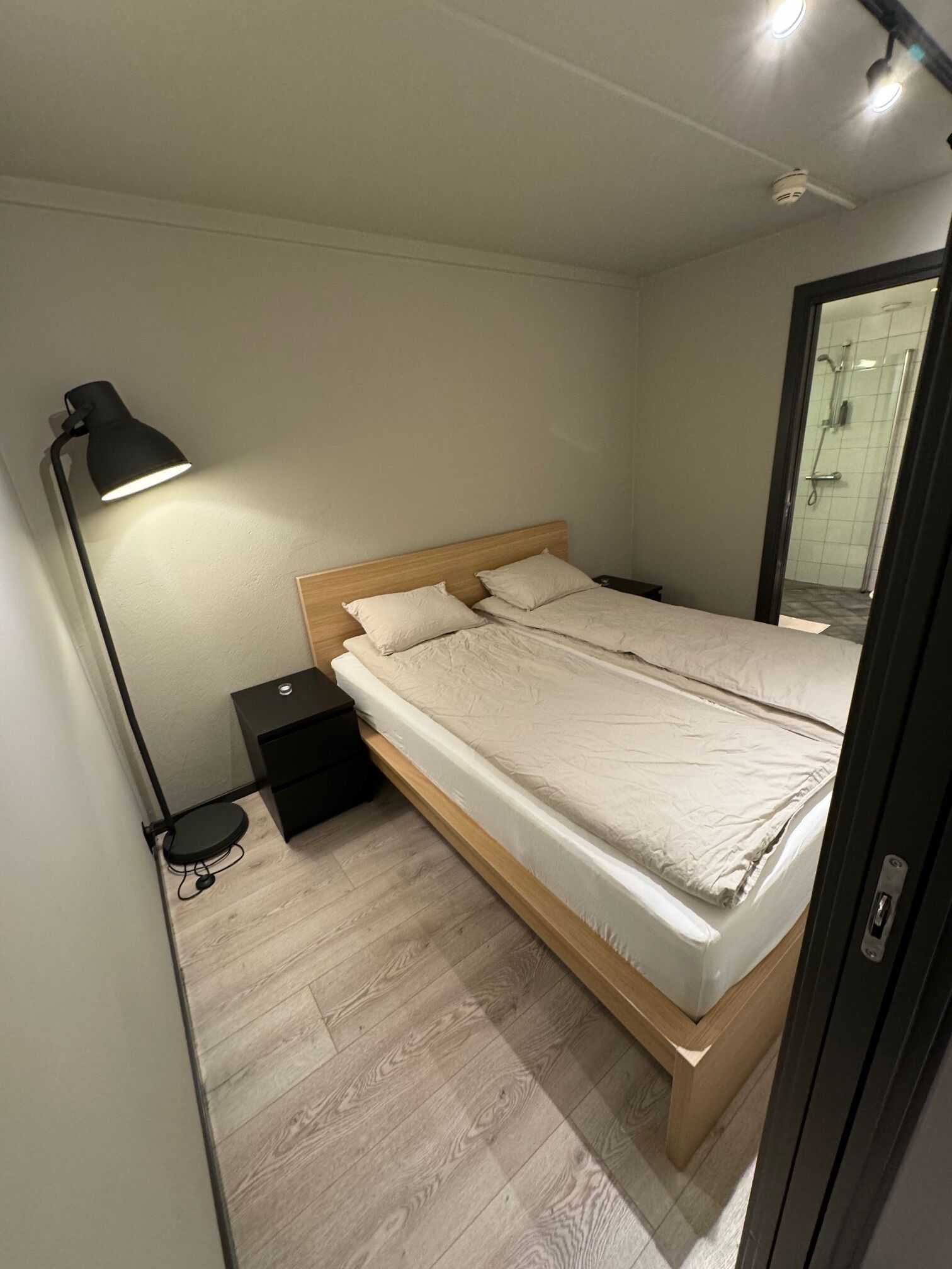 Una camera da letto con un letto, un comodino, una lampada e una porta che dà su un bagno.