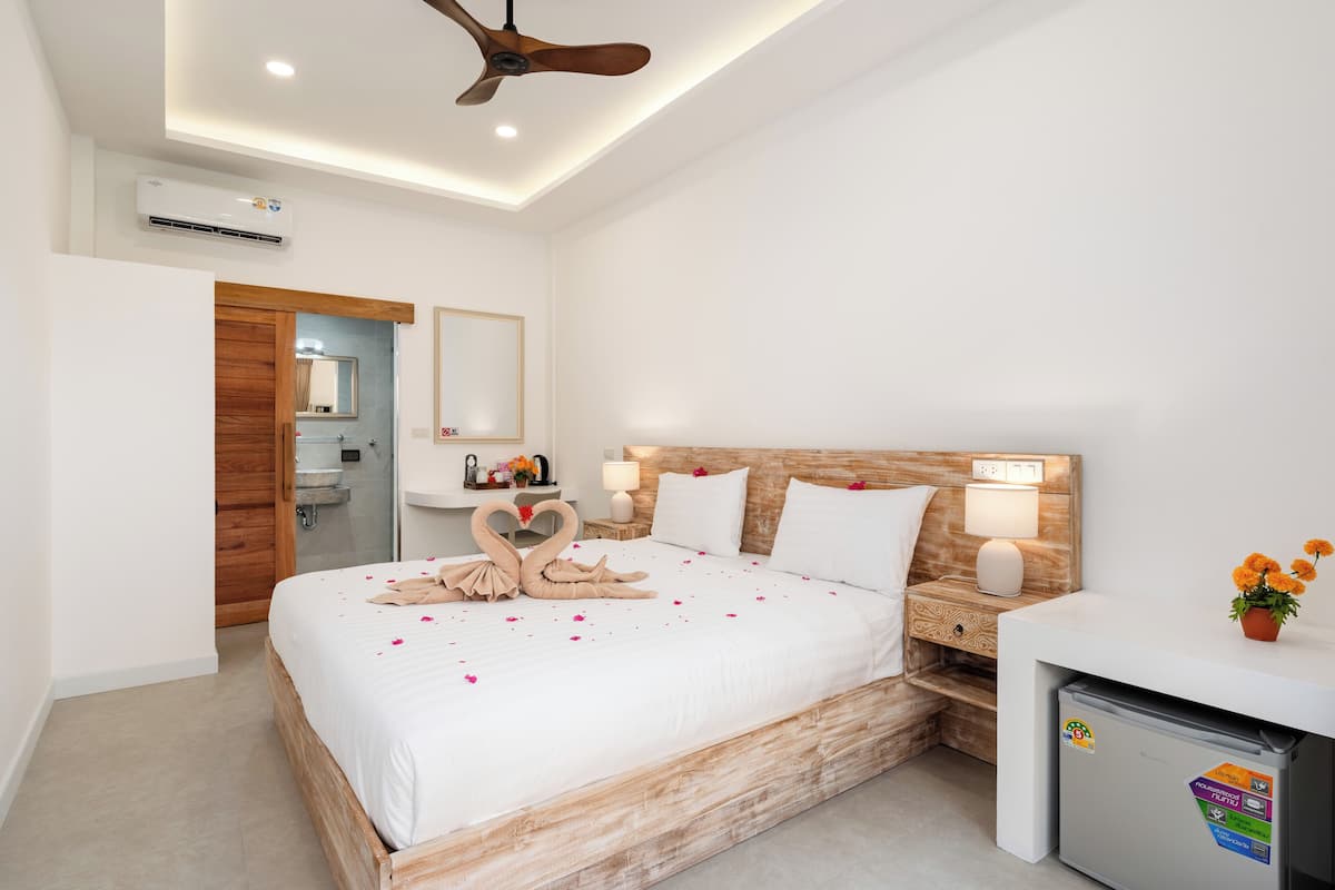 Una camera d'albergo moderna con un letto a telaio in legno, una scrivania integrata, una ventola a soffitto e un piccolo frigorifero.