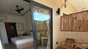 A hotel room with a sliding glass door leading to a balcony, a bed, a desk, and a chair. - Eden Extend Fisherman Village (Koh Samui)