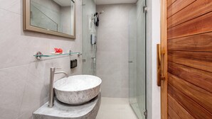 A modern bathroom with a glass shower enclosure, a marble sink, and a wooden door. - Eden Extend Fisherman Village (Koh Samui)