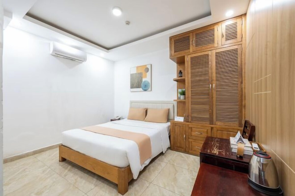 A bedroom with a bed, wooden wardrobe, and a desk with a kettle.