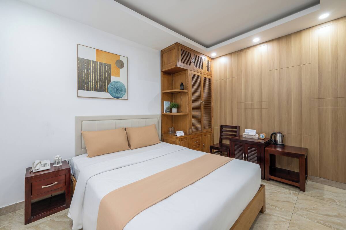 A neatly arranged hotel room with a bed, bedside tables, a wooden wardrobe, and a small desk with a chair.
