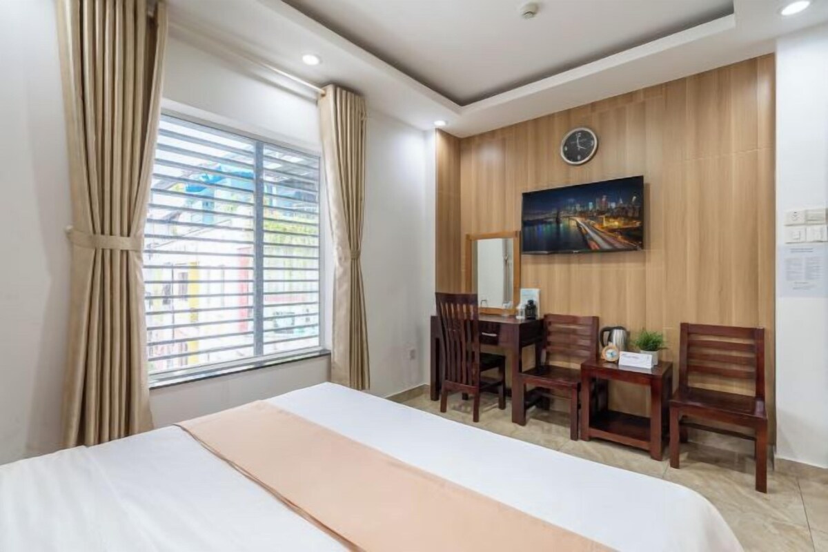 Habitación de hotel con cama, escritorio, dos sillas, un reloj en la pared y ventana con cortinas.