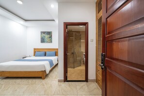 Una habitación de hotel con una cama de madera, una puerta de ducha de vidrio y un armario de madera.